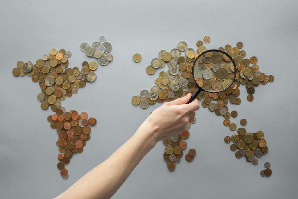 pexels photo 7412098 7412098 1 Top view of crop unrecognizable traveler with magnifying glass standing over world map made of various coins on gray background